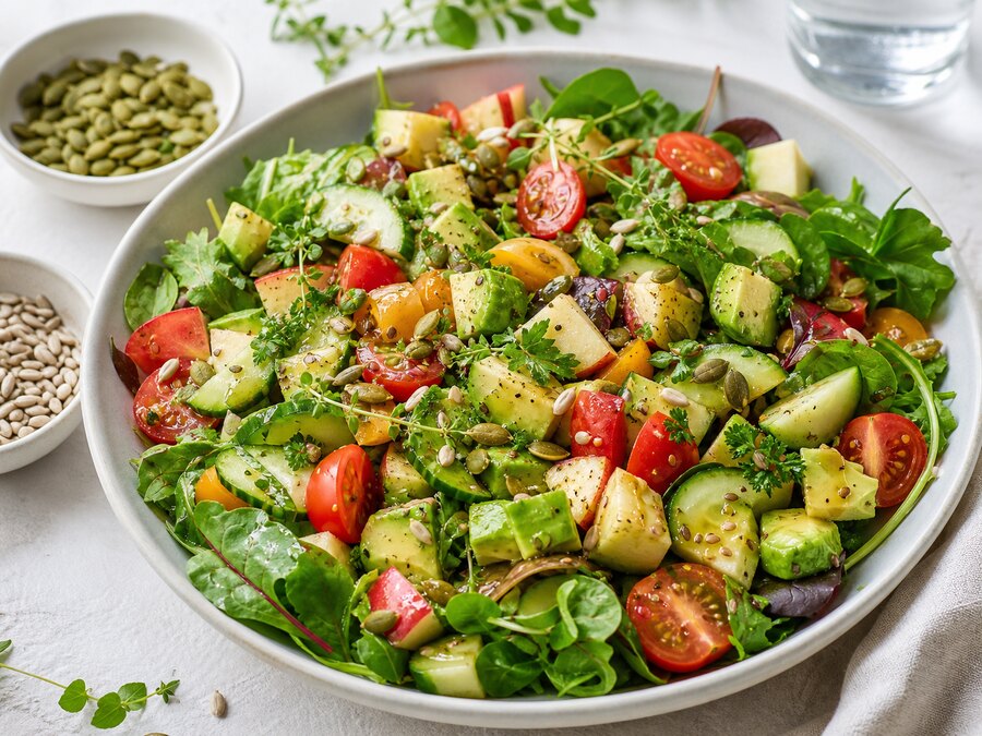 Färgstark sallad med gröna blad, gurka, tomat, avokado, äpple och frön